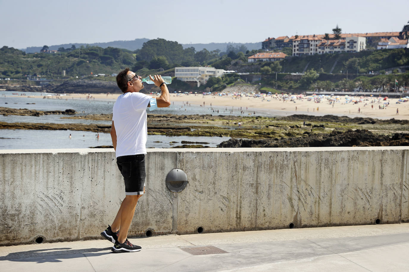 Un hombre se refresca en el paseo de la playa, en Comillas