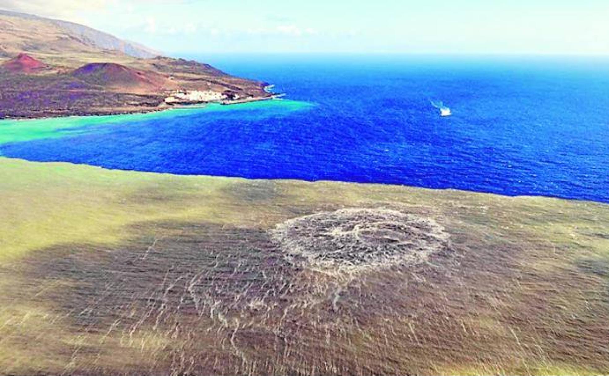 Mancha generada durante la erupción del volcán Tagoro en la superficie del mar. Al fondo, a 1,8 kilómetros de distancia, la localidad de La Restinga, que tuvo que ser desalojada.  