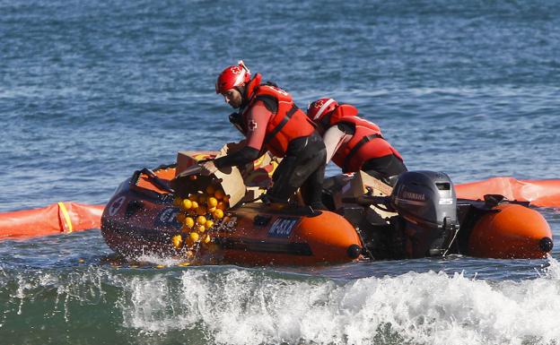 Miembros de Cruz Roja que participaron este jueves en el ejercicio tiran naranjas al mar. Las frutas flotan y simulan el vertido de hidrocarburo.