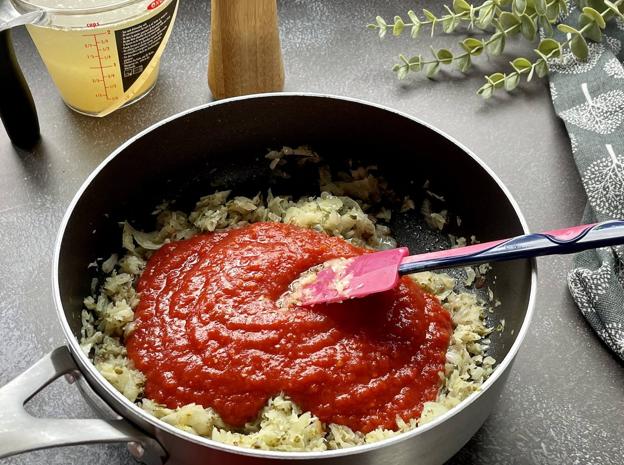 Una vez rehogada la cebolla, añadir la pulpa de tomate y la mitad del caldo.