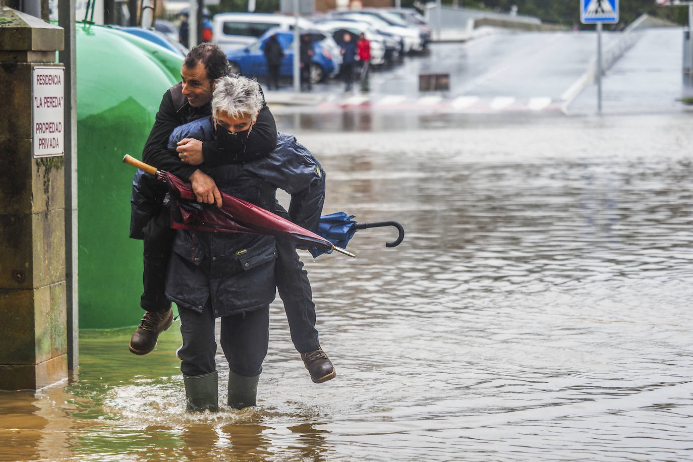 Un hombre ayuda a otro a cruzar una balsa de agua tras las inundaciones en Ampuero.