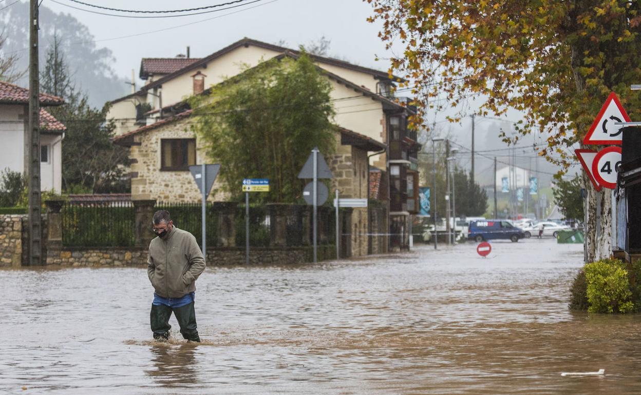 Un hombre camina por la calle de El Puente, en Oruña de Piélagos, con el agua hasta la rodilla en las inundaciones del lunes.