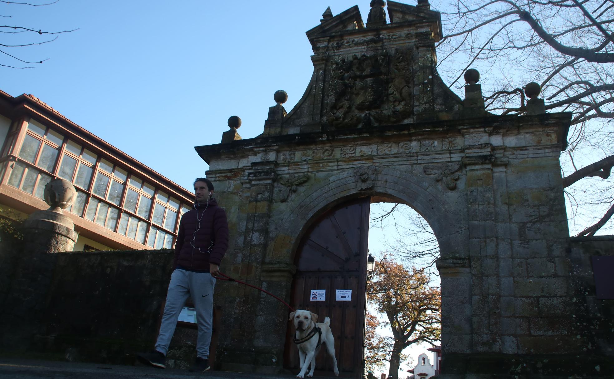 Un hombre pasea con su perro junto a la portalada de acceso a la  finca, que va a ser rehabilitada 