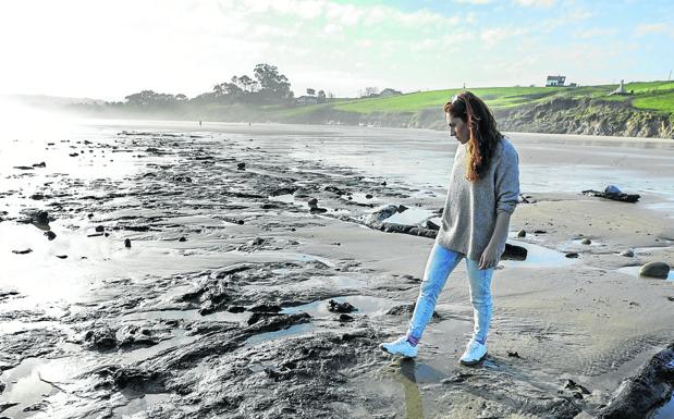 Una chica observa los troncos sobre la arena de la playa de Oyambre. 