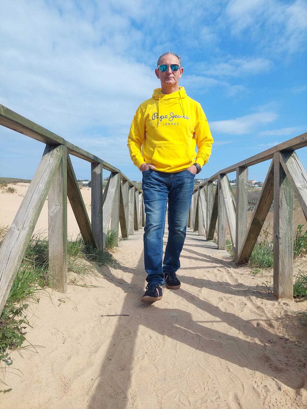 Sudadera con capucha en amarillo intenso, con vaqueros de un tejido suave, deportivas y gafas de espejo.