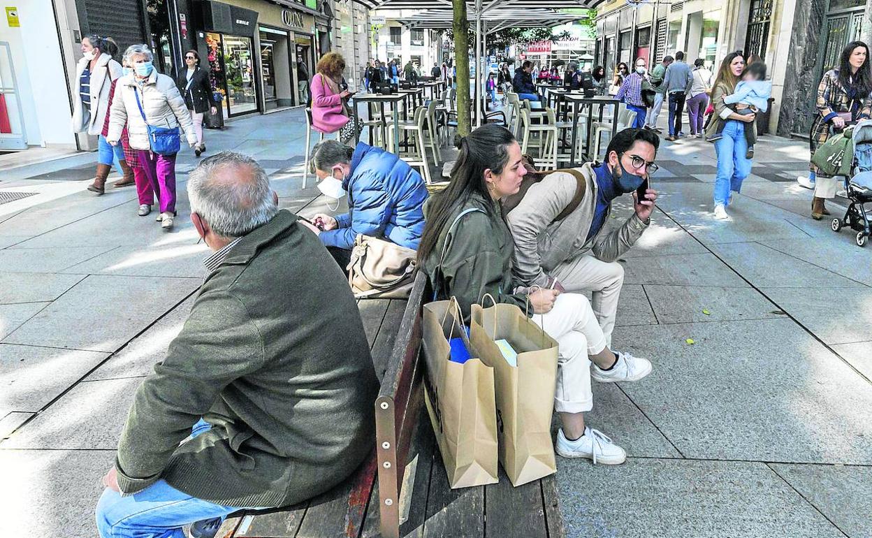 Un grupo de personas ocupa un banco mientras otras pasean por una calle del centro de Santander. 