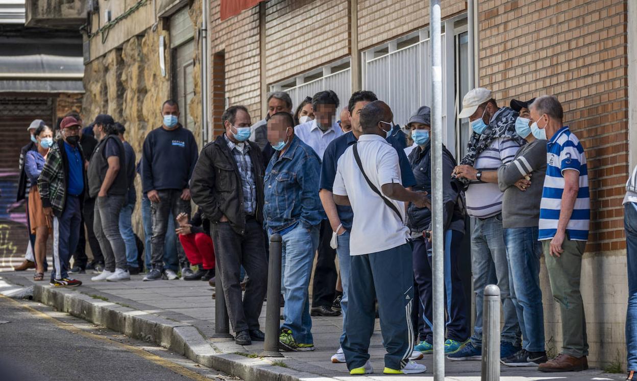 Decenas de personas, este jueves al mediodía, hacen cola a las puertas de la Cocina Económica, en Santander, mientras esperan su turmo antes de entrar al comedor. 