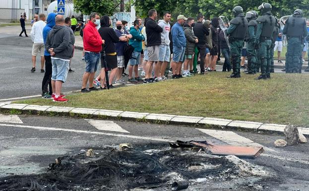 Restos de las barricadas apagadas en Guarnizo por los bomberos en primer plano y trabajadores y Policía al fondo.