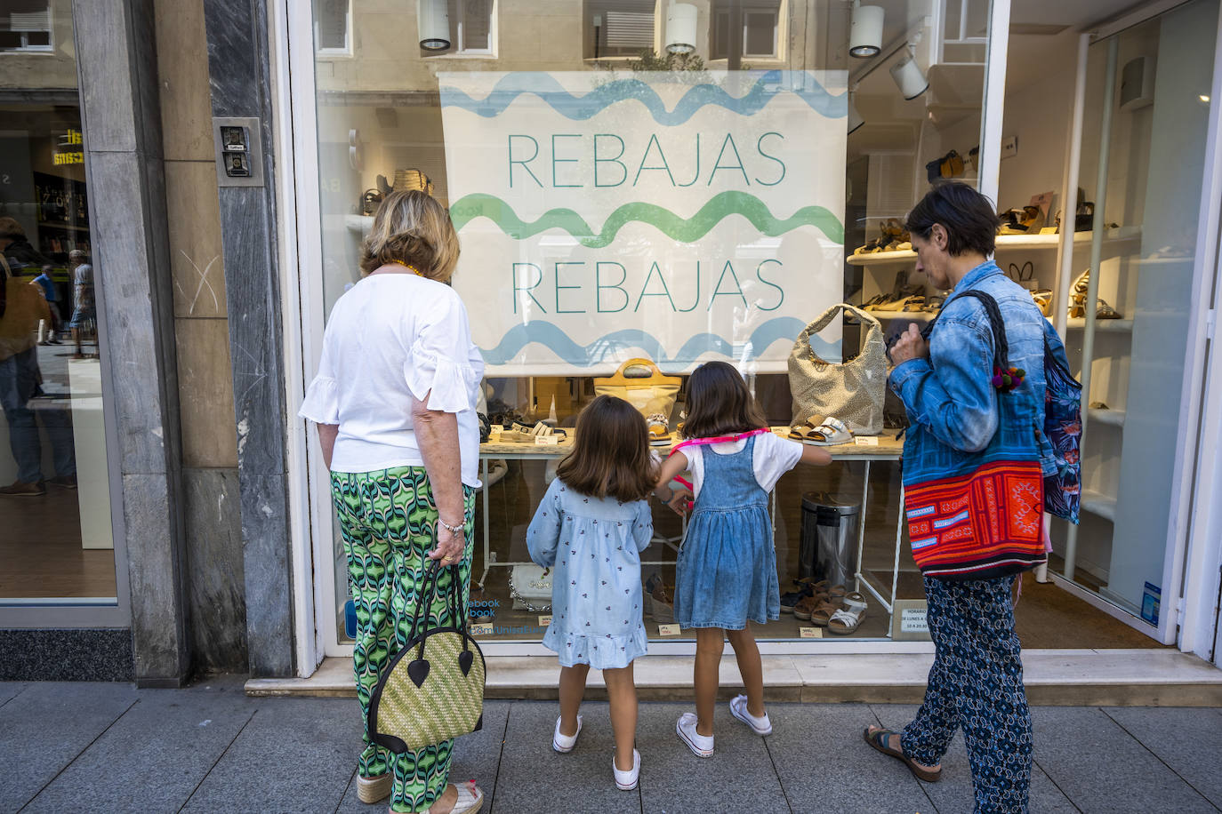 Imagen secundaria 1 - Arriba, una mujer observa el escaparate de la tienda Azul, en la calle Lealtad. Abajo, dos mujeres y dos niñas miran calzado y una mujer, en el interior de una tienda de ropa.