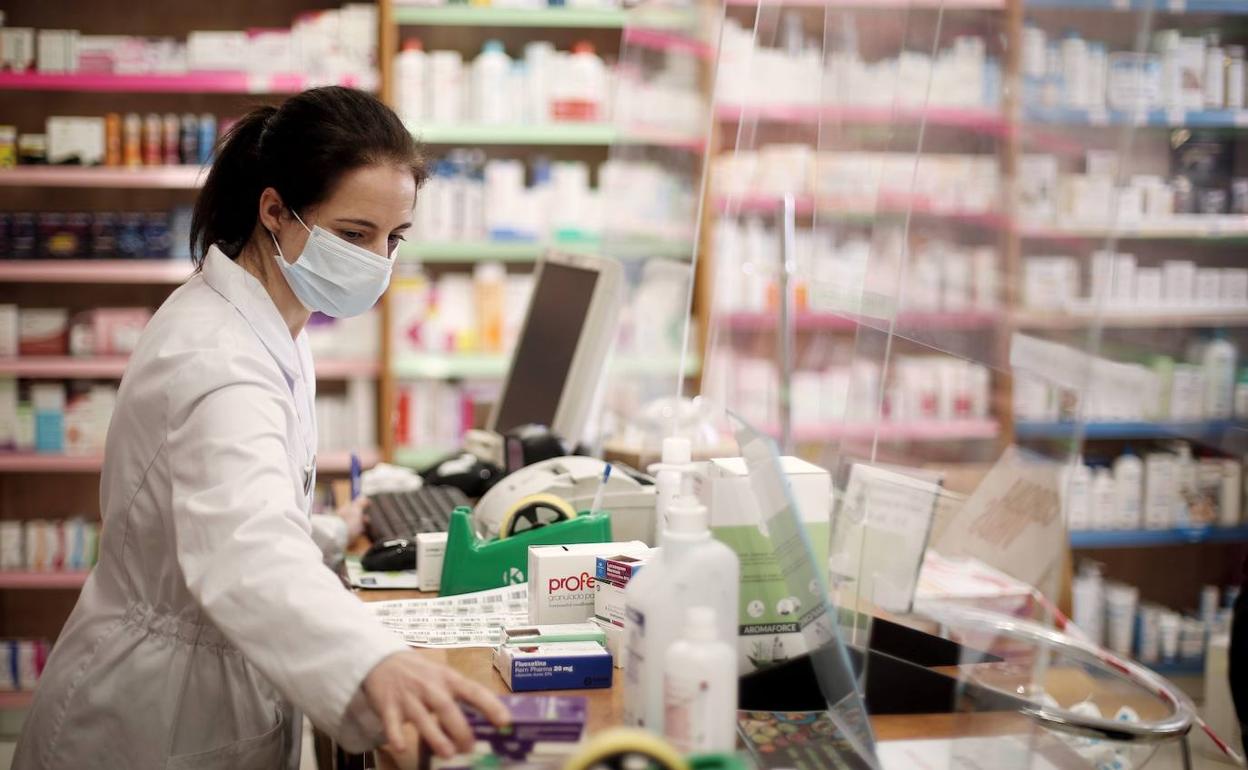 Una farmacéutica despacha en su establecimiento con mascarilla.