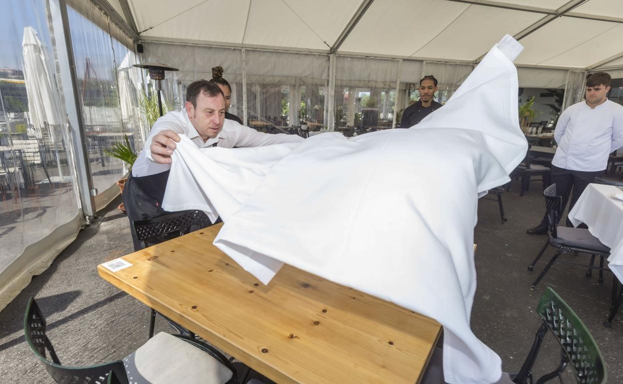 Un trabajador de hostelería prepara una mesa en una terraza antes de empezar con el servicio de comidas. 