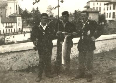 Imagen secundaria 1 - A la izquierda, Celedonio Pérez Abascal, «Lonio el molinero» con una buena pieza de salmón, flanqueado por dos guardarríos. La pose tiene como fondo el puente sobre el Pas y el Balneario de Puente Viesgo, en los años 50 del Siglo XX. A la derecha, un pescador en el río Pas, en los primeros años del Siglo XX. Usando la técnica propia de aquellos años: vara y butrón de mano.