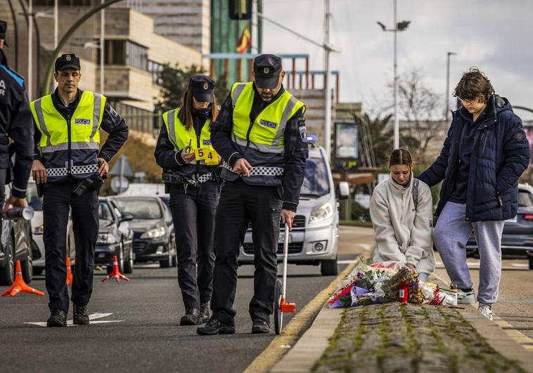 Dos compañeros de colegio del motorista arrollado en Castelar depositan unas flores en el lugar del accidente mientras los policías analizan la zona