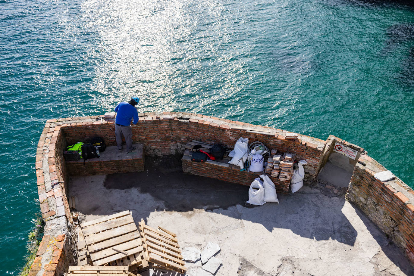 Un trabajador repara el muro perimetral que rodea la explanda de acceso al faro.