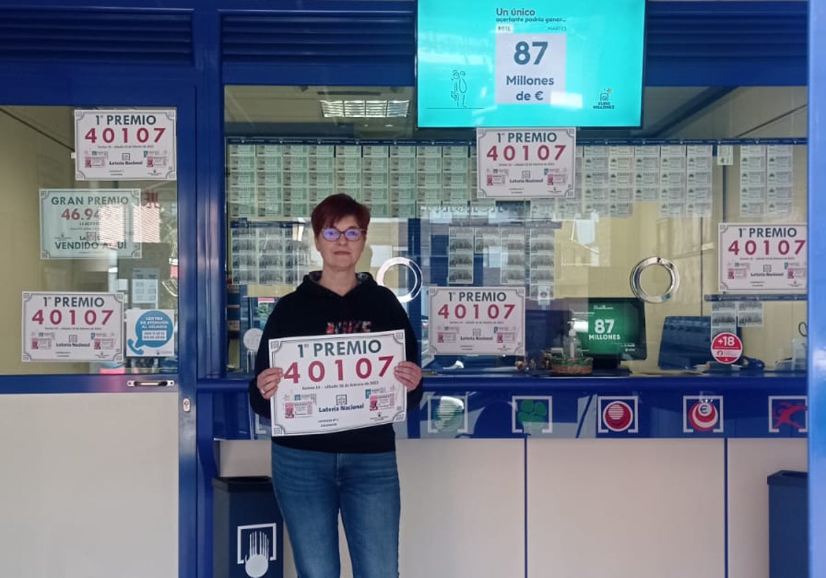 Natalia Sañudo posa con el cartel que acredita a la administración de loterías que regenta en Colindres junto a su hermano, Alejandro, como punto de venta del primer premio.