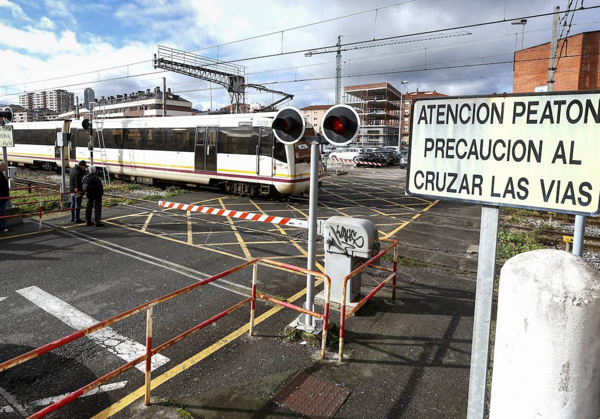 Vecinos esperan en el paso a nivel de Pablo Garnica, durante la salida de un tren de Cercanías hacia Santander.