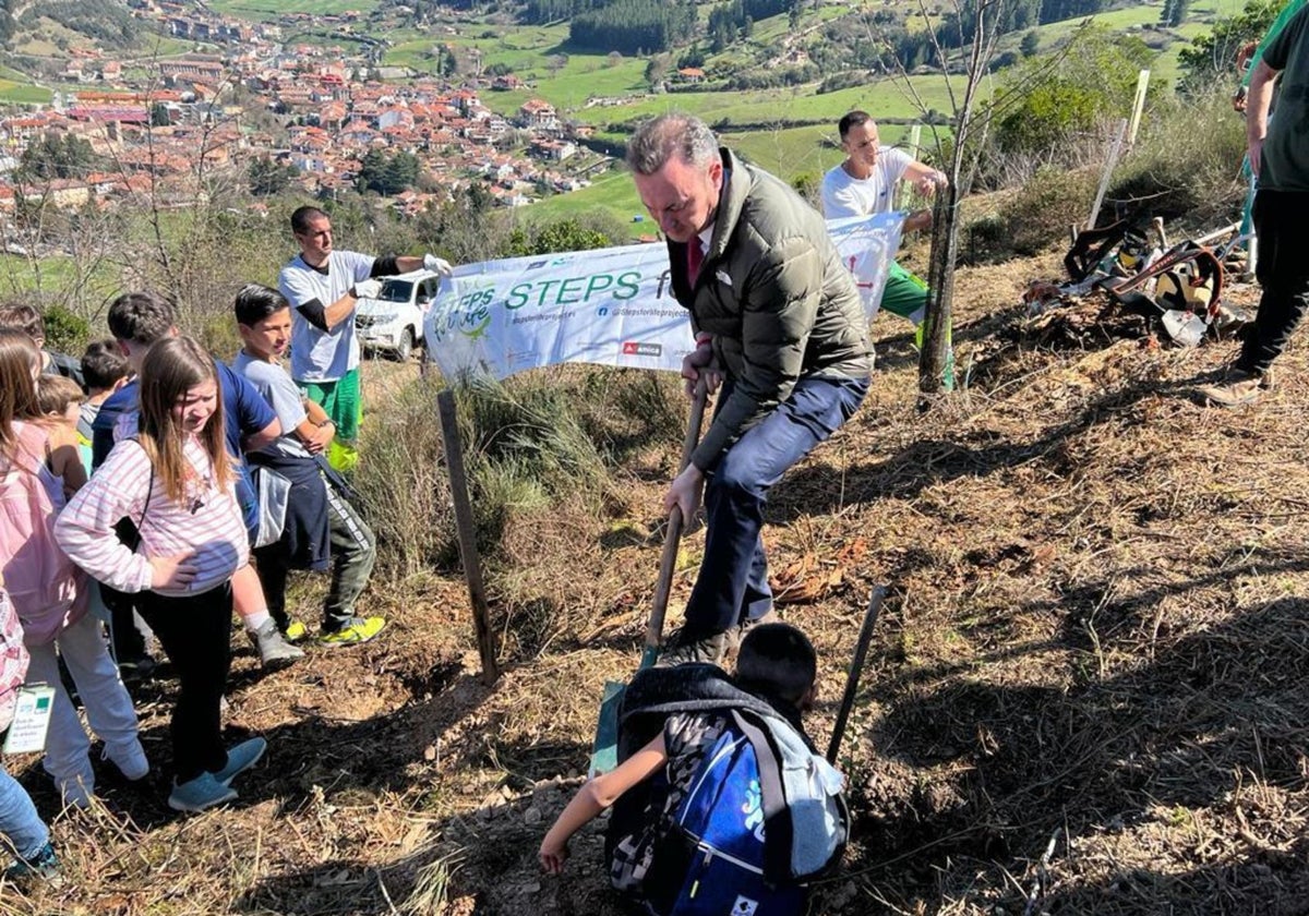 Guillermo Blanco y un escolar del CEIP Concepción Arenal plantan un árbol en el monte Viorna, con el fondo de la villa de Potes