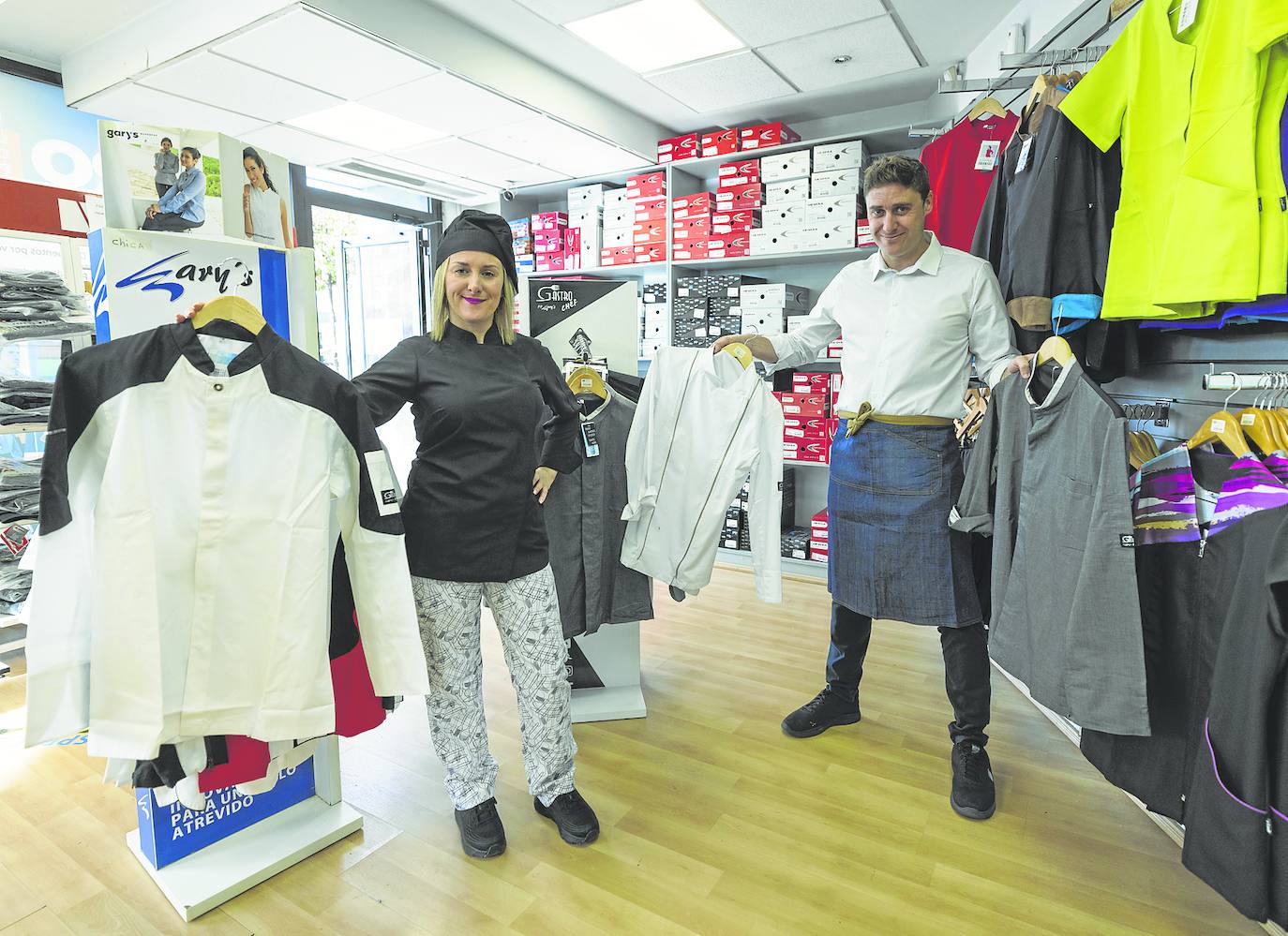 Elena Galdós, empleada, y Óscar Ojea, en la tienda de La Albericia, muestran algunas de las chaquetillas. Elena viste chaquetilla y gorro negros, pantalón estampado y zapatillas con máximo nivel de agarre.