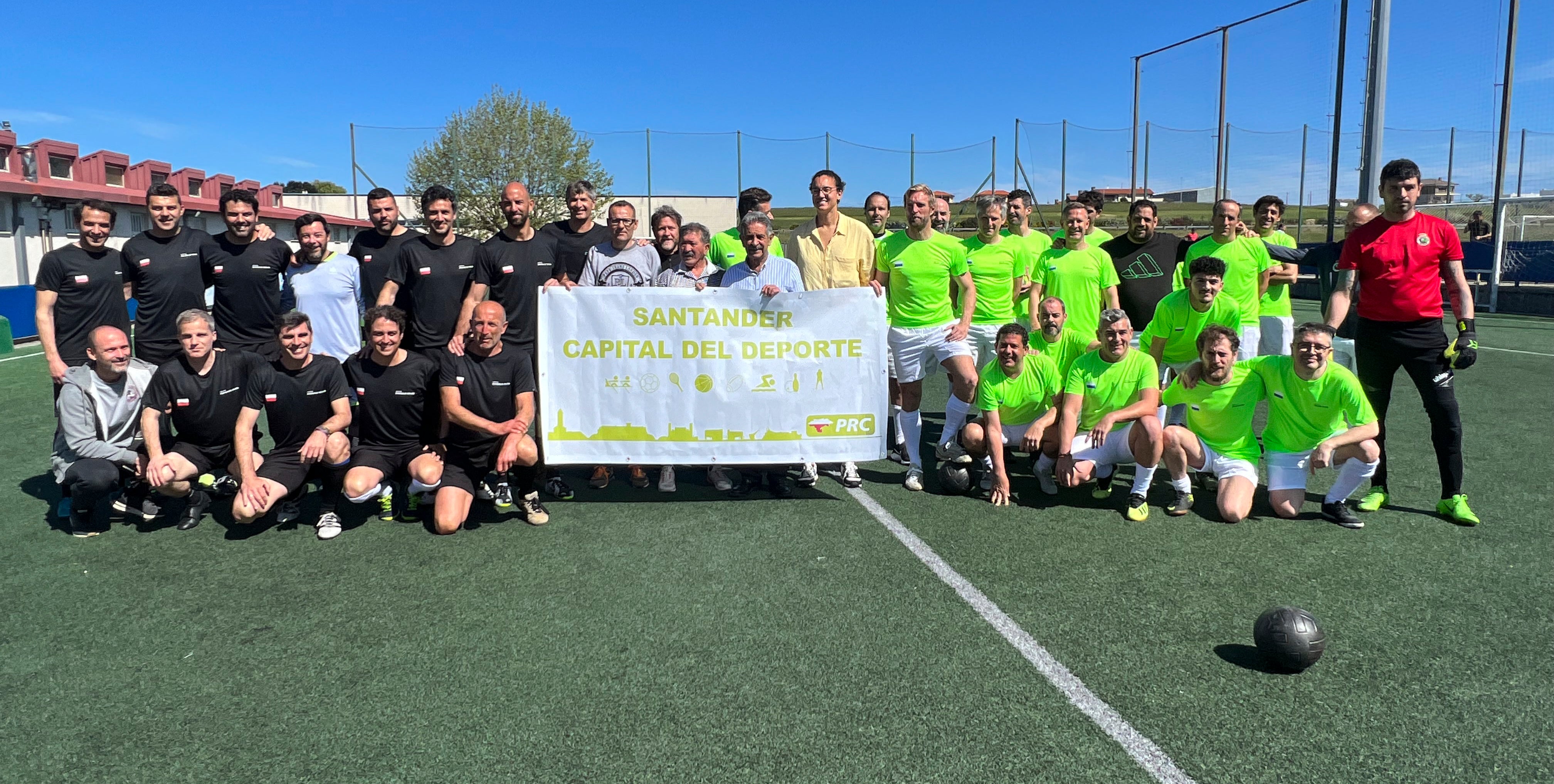 Foto de familia de los dos equipos (de verde, el de piña, y de negro, el de Colsa), antes del Partido, con  Miguel Ángel Revilla en el centro.