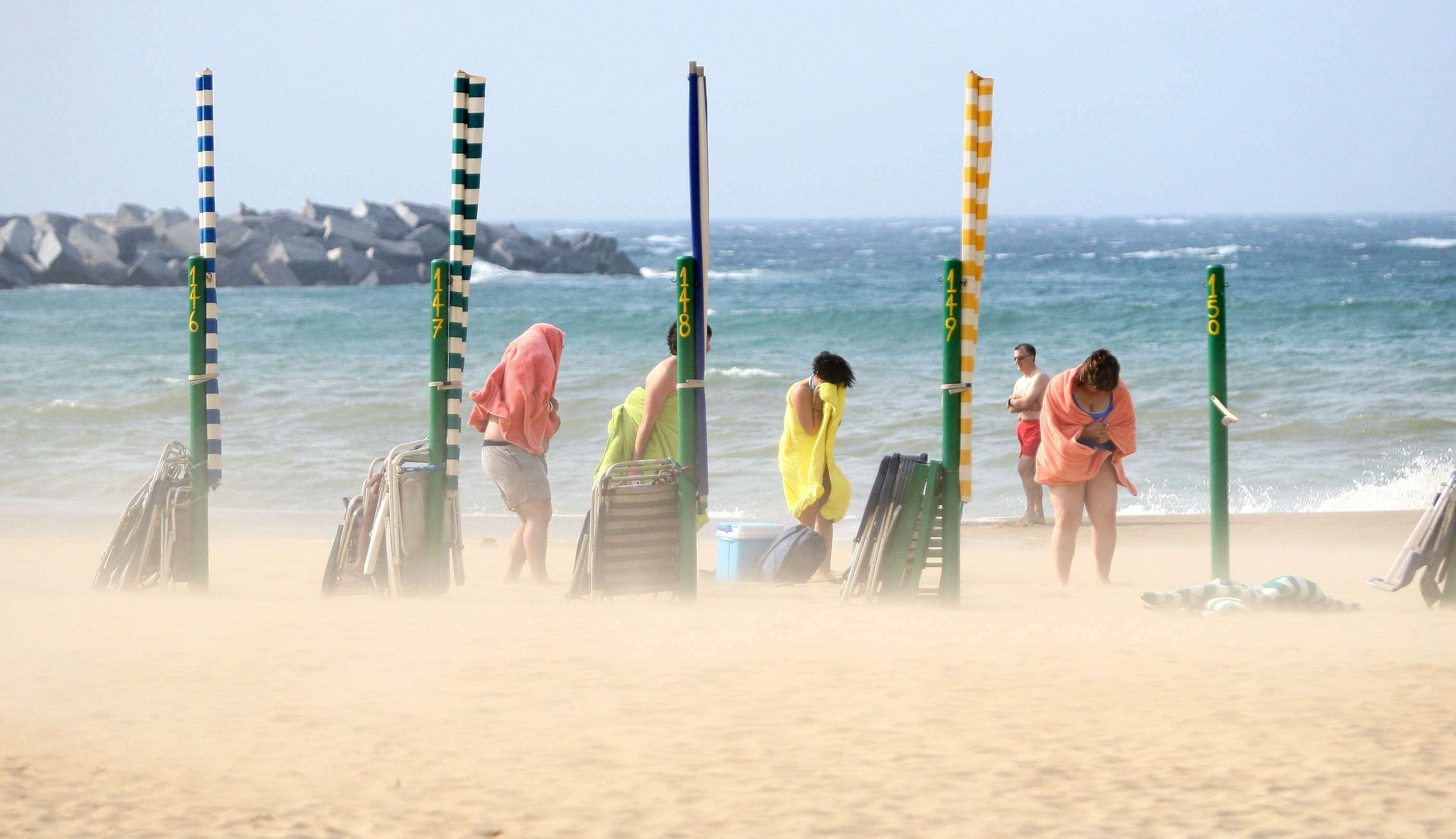 Bañistas se protegen del fuerte viento y la arena en una playa del norte de España.