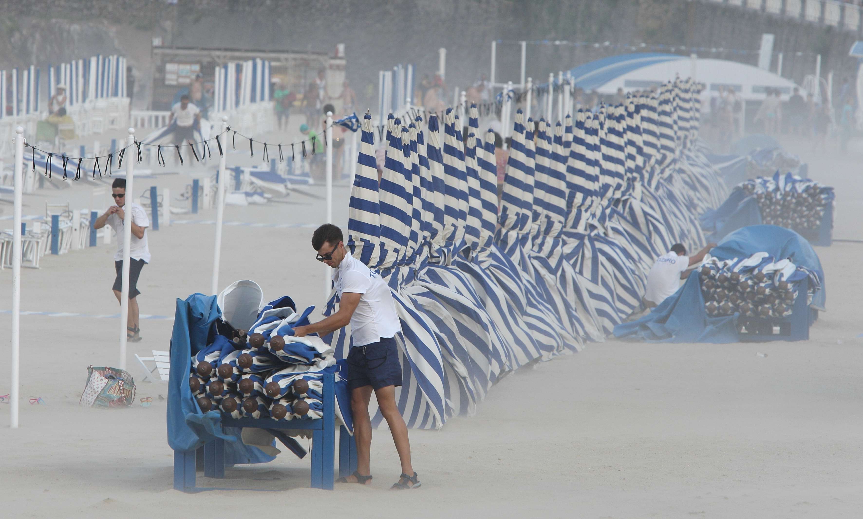 Dos trabajadores recogen con dificultad por el fuerte viento las sombrillas de una playa del País Vasco.