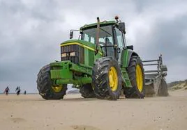 Un tractor limpia la playa de Somo para retirar material vegetal traído por la marea y otros restos de basura.