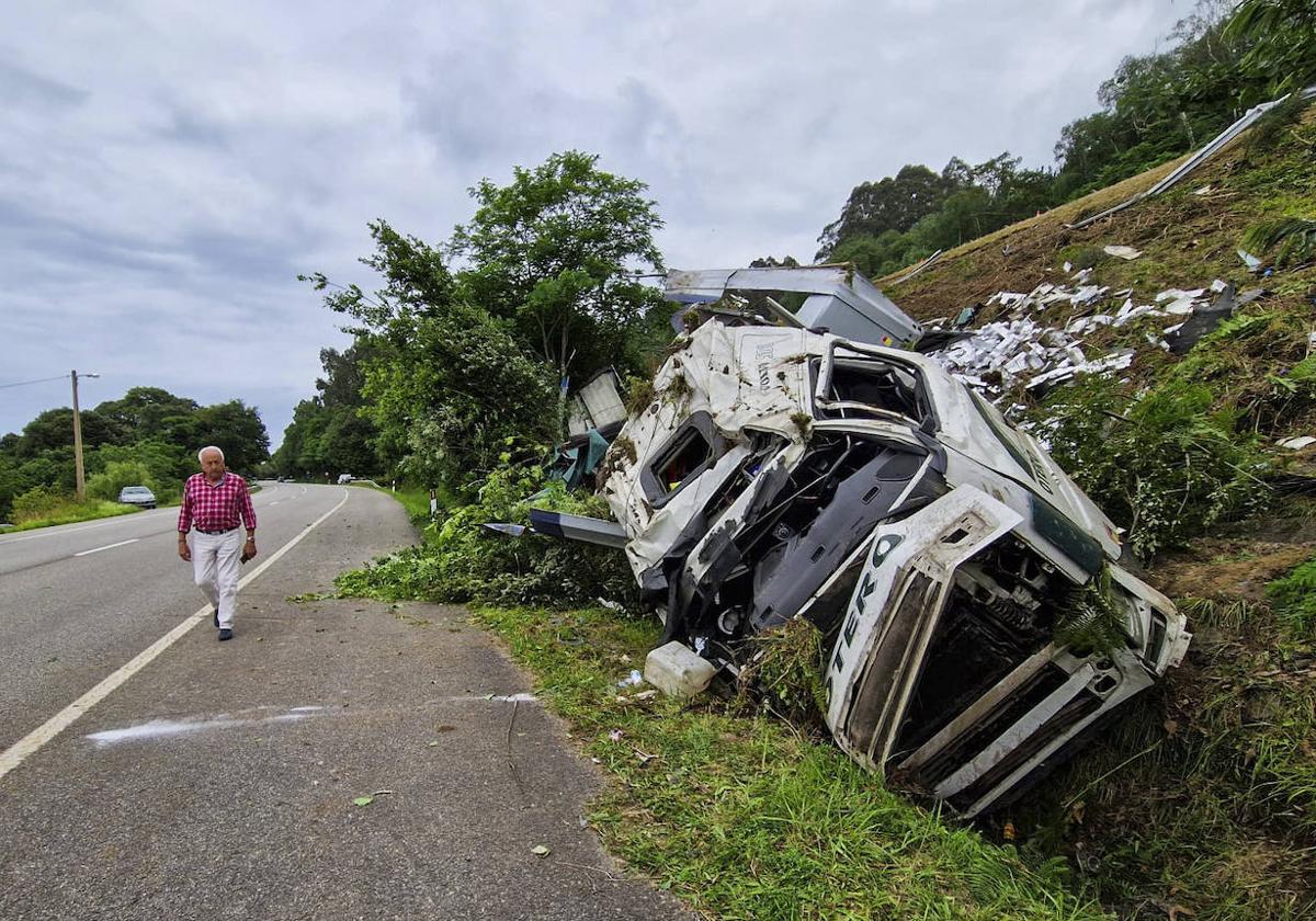 Un vecino camina junto a los restos del camión accidentado en la localidad asturiana de Buelna.