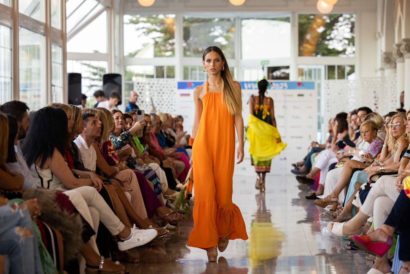 María Fernanda desfila con un vestido largo naranja con unas zanahorias en la mano.