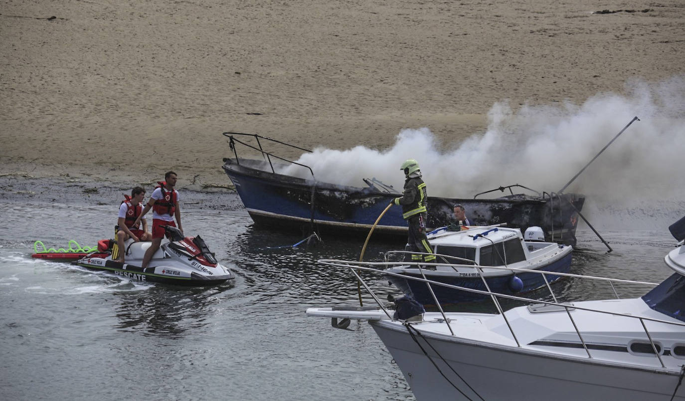 Los miembros de rescate de la Cruz Roja hablan con un bombero tras extinguirse las llamas del barco