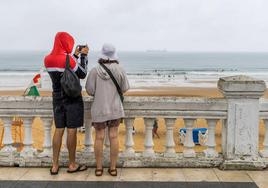 Una pareja, protegida de la lluvia con gorro y capucha, fotografía a los surfistas en El Sardinero