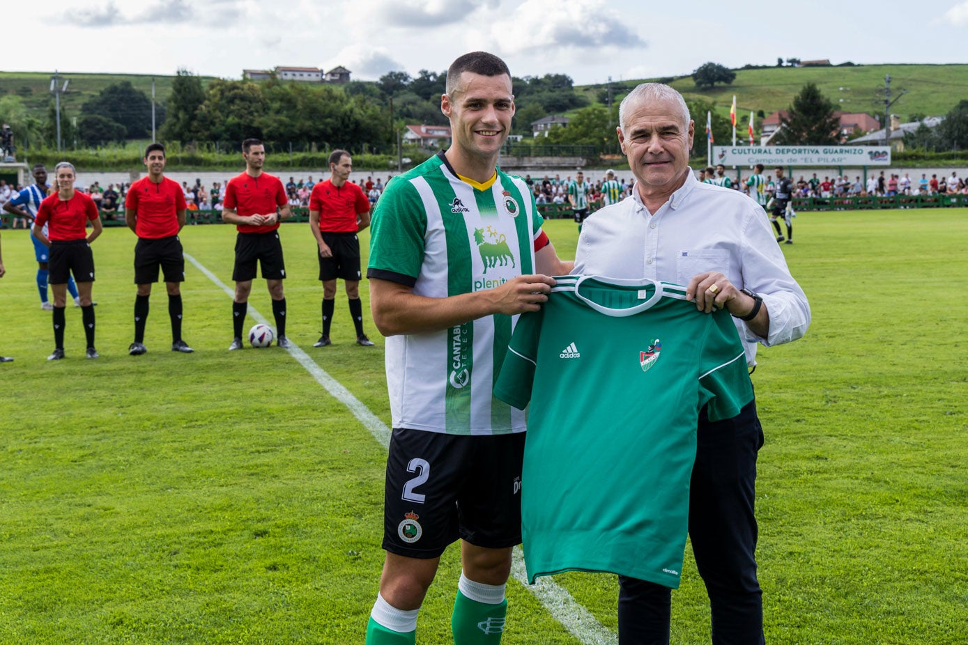 El jugador del Racing Álvaro Mantilla recibe una camiseta de manos del presidente de la Cultural de Guarnizo, José Luis López.