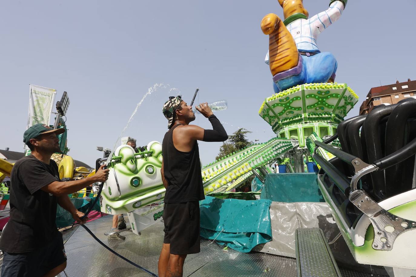 Los feriantes que montan las atracciones de cara a las fiestas de La Patrona de Torrelavega se refrescan del calor con una manguera.