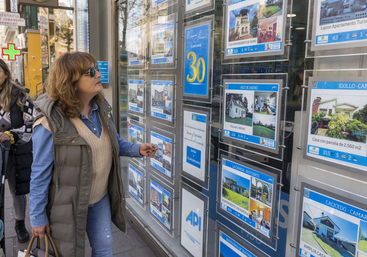 Una mujer mira viviendas en venta en el escaparate de una inmobiliaria de Santander.