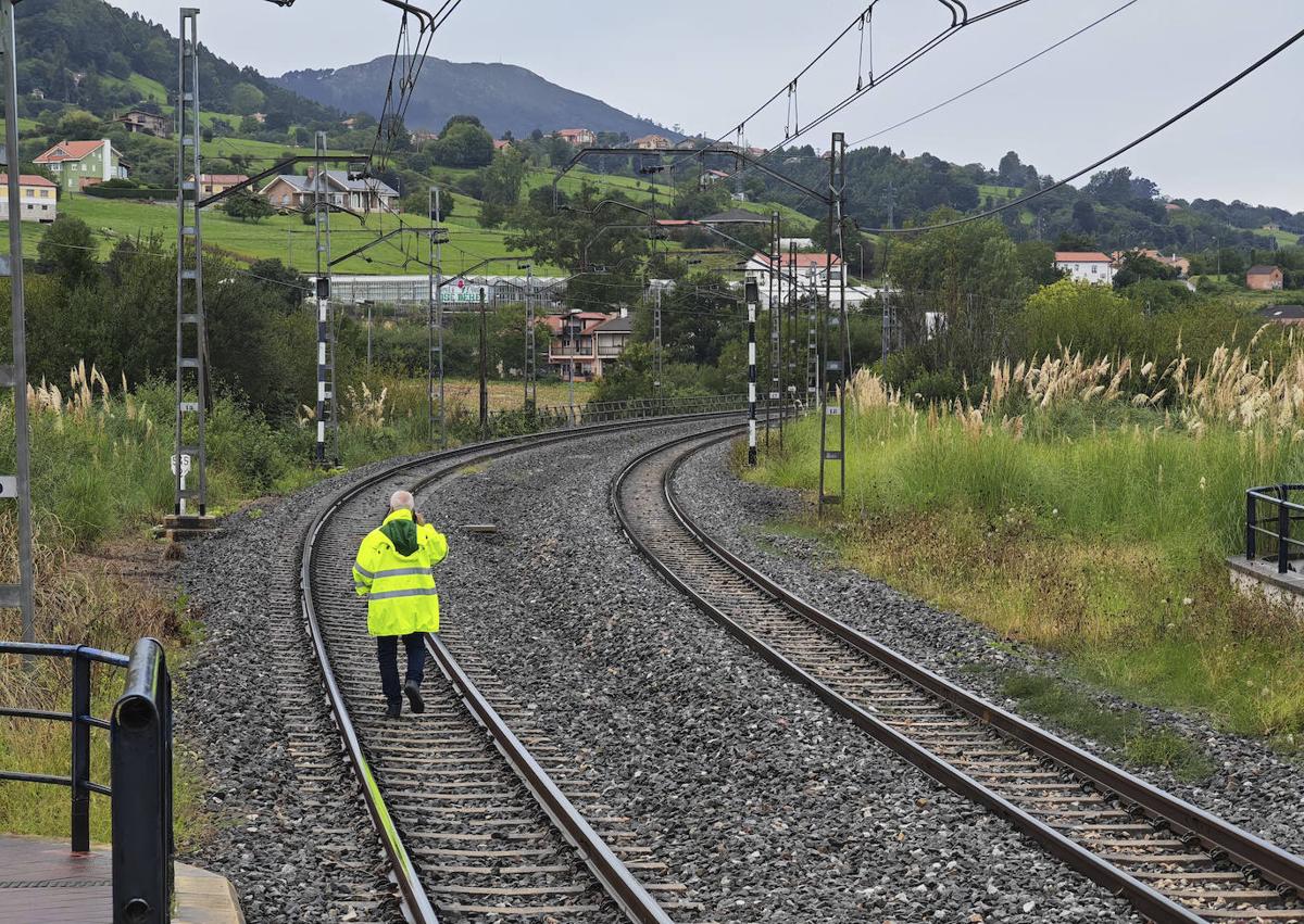 Imagen secundaria 1 - Un operario de Adif, con chubasquero fluorescente camina por la vía hacia el tren descarrilado. Al lado, unos pasajeros se disponen a cruzar el paso de cebra para subir al autobús que les lleva hacia Liérganes. 