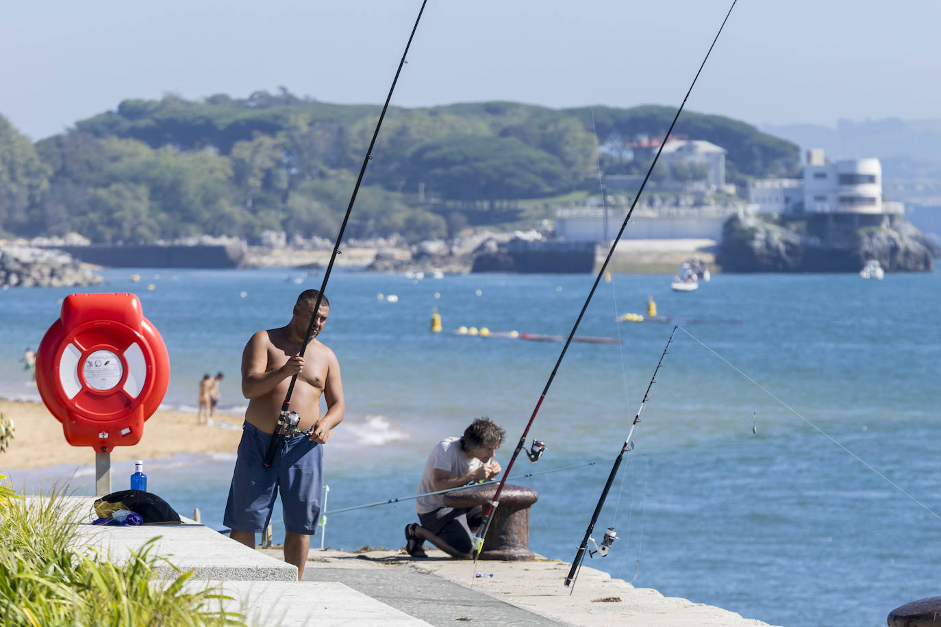 Dos hombres preparan sus cañas antes de pescar cerca de la playa de Los Peligros de Santander.