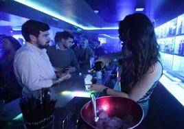 Una camarera sirve una copa a unos clientes en una discoteca.