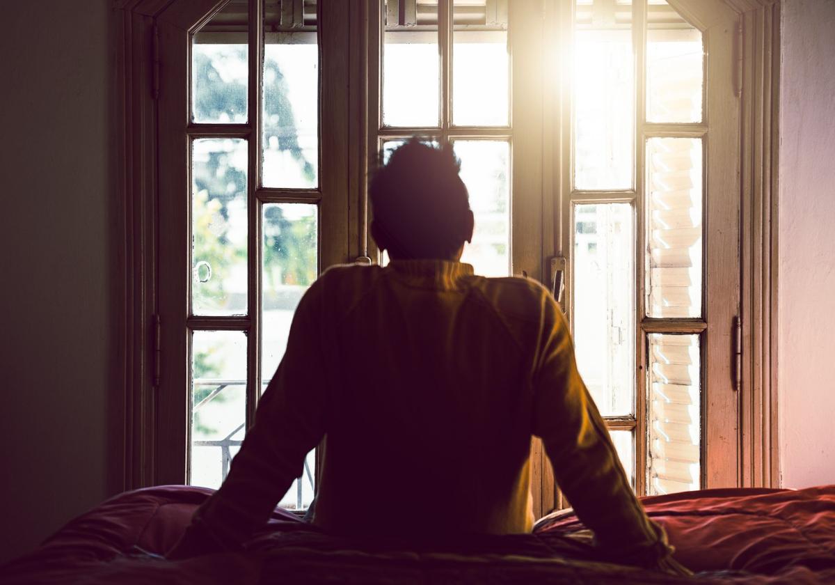 Un joven mira por la ventana de espaldas.