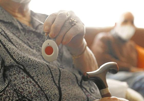 Una mujer mayor muestra su medalla de teleasistencia.