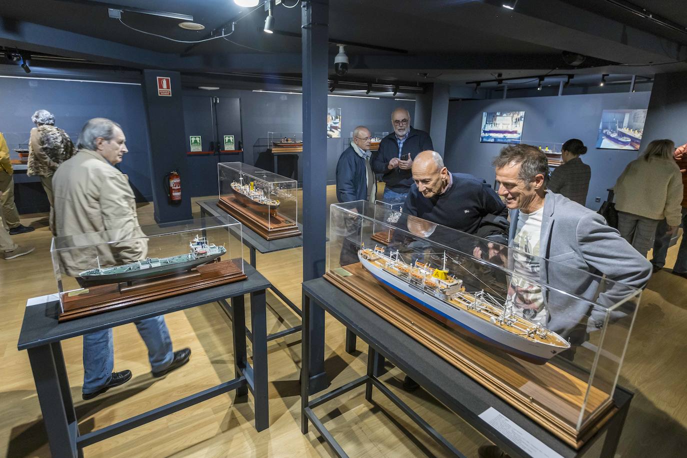 Varias personas observan las muestras de la exposición dedicada a los barcos que han recalado en el Puerto de Santander.