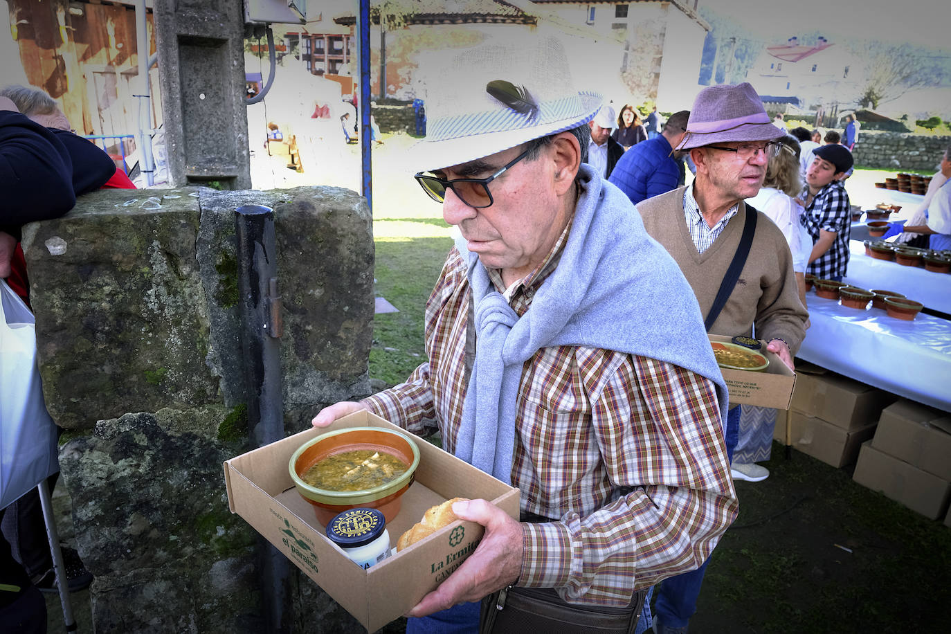 Un señor se protege del sol con un gorro tras recoger su ración de cocido. 