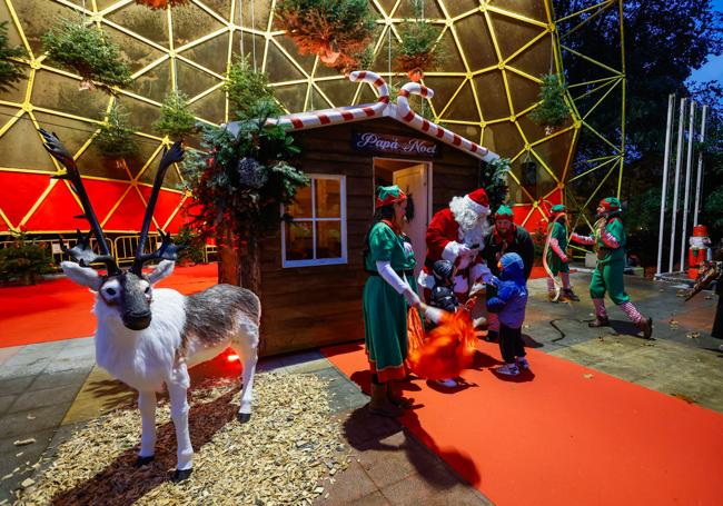 Familias hacen cola frente a la cabaña de Papá Noel custodiada por sus ayudantes, este lunes, en el parque Manuel Barquín de Torrelavega.