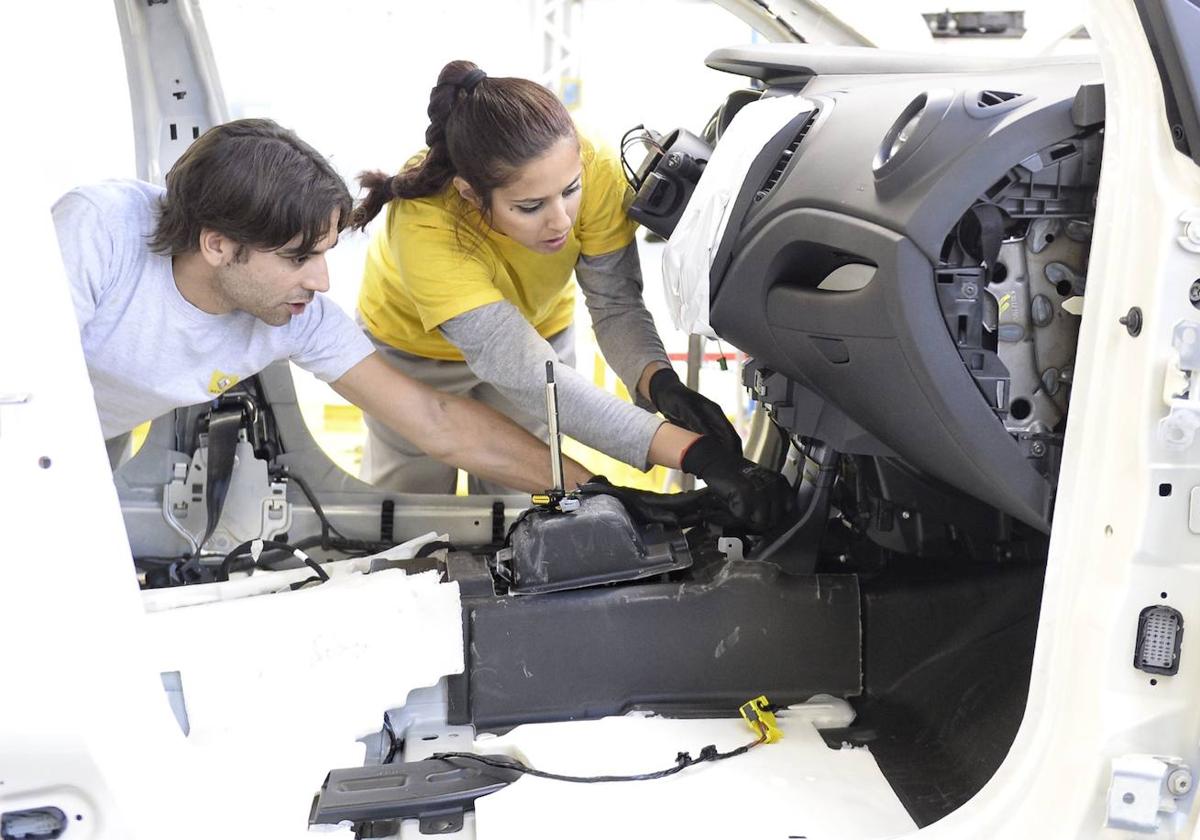 Un hombre y una mujer trabajan en el montaje de las piezas de un automóvil.