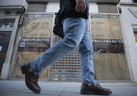 Un hombre camina ante un negocio con un cartel de próxima apertura en Santander.