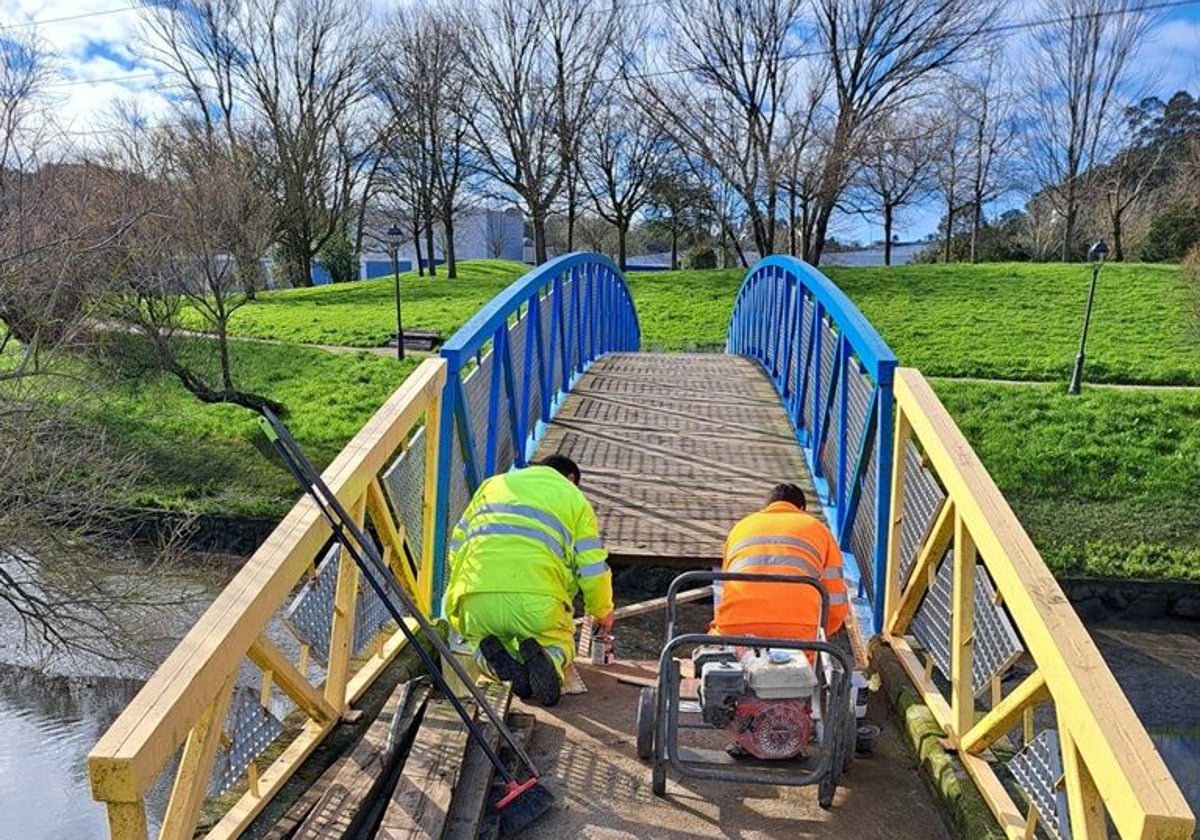 Dos operarios sustituyen la madera del puente peatonal sobre la ría del Carmen.