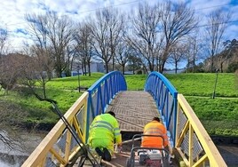 Dos operarios sustituyen la madera del puente peatonal sobre la ría del Carmen.