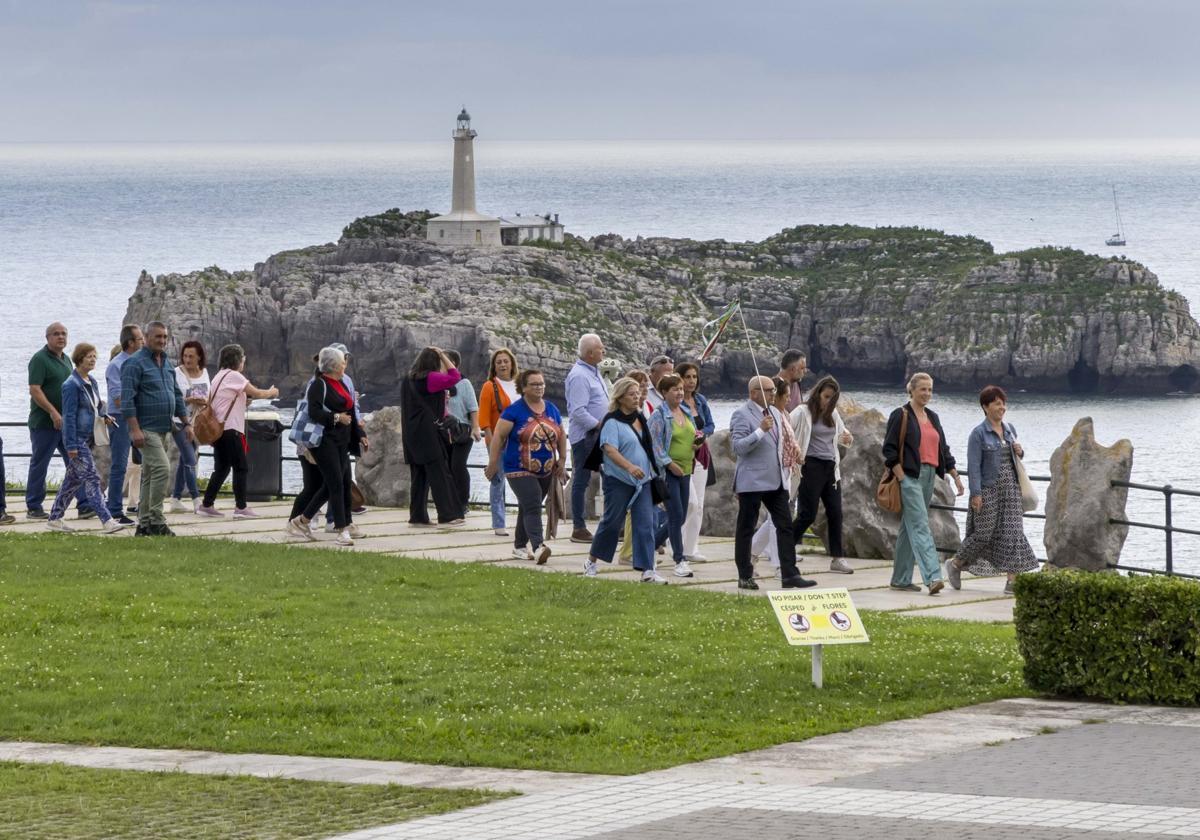 Un grupo de turistas visita el entorno del Palacio de La Magdalena, con el faro de Mouro al fondo.