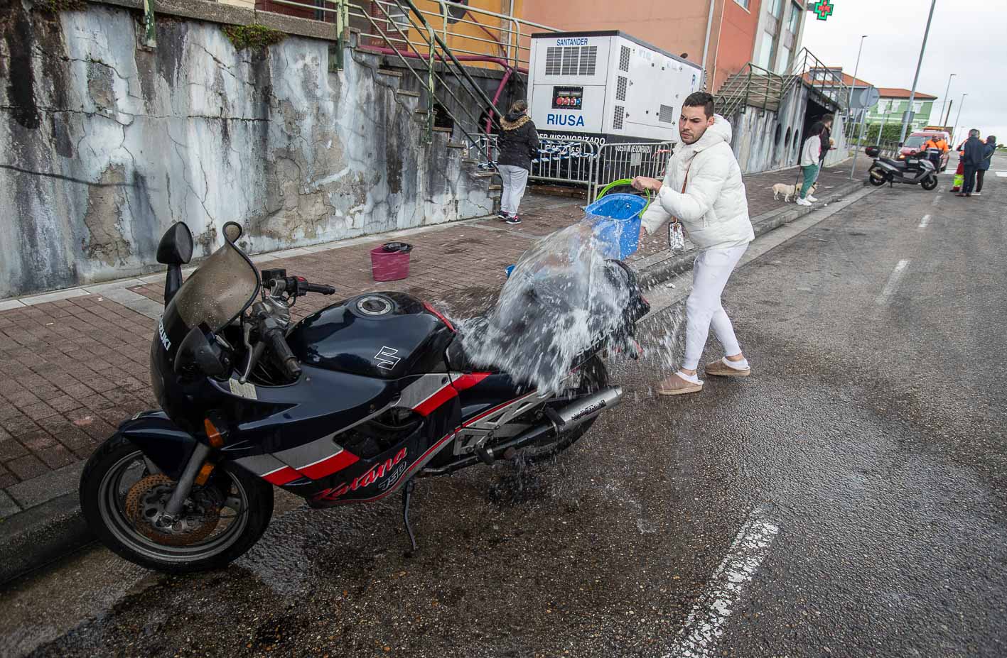 Otro residente limpia su moto con calderos de agua. 