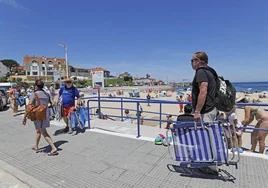 Bañistas atraviesan el paseo marítimo de la playa de Comillas en verano.