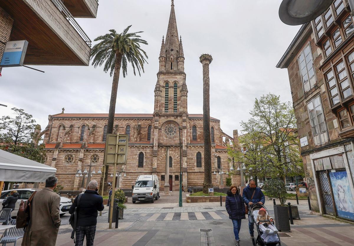 Vecinos caminan frente a las palmeras de La Asunción, una de ellas sin hojas, en Torrelavega.