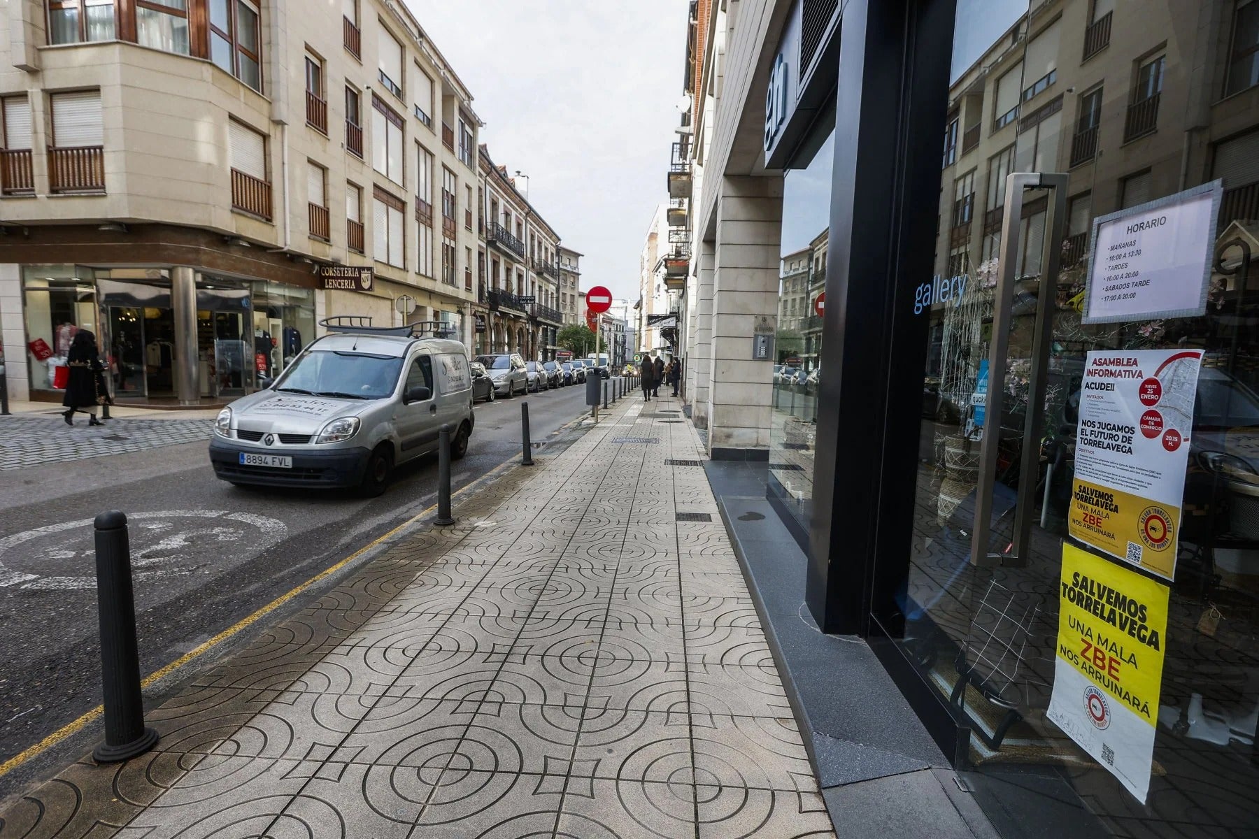 Un coche circula por la calle Joaquín Hoyos frente a un escaparate con carteles contra la ZBE.